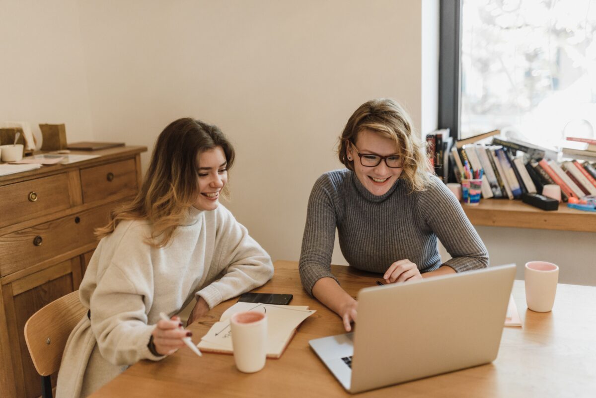 Två kvinnor som sitter och tittar in i en laptop och ler | NTI-skolan